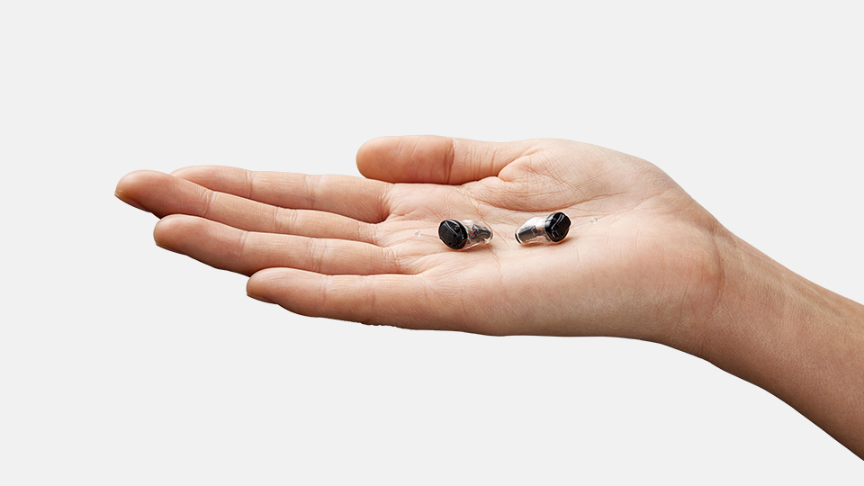 Hand holding IIC Oticon Own hearing aids in palm