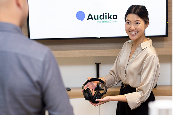 Audika staff handing client headphones for a hearing test