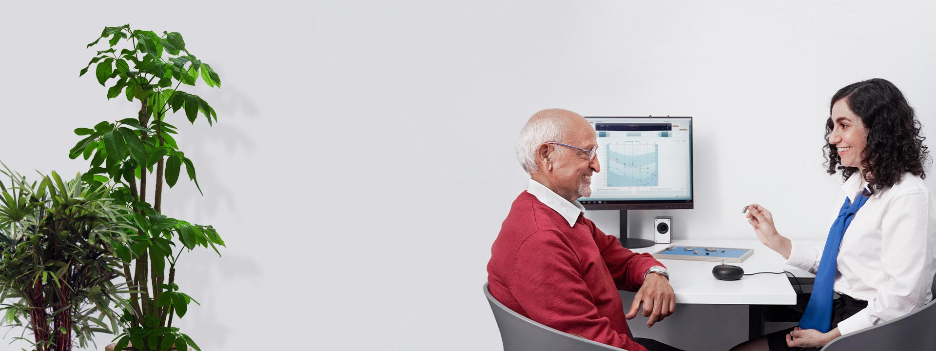 Image shows an audiologist talking to a person with hearing loss  in front of a screen showing an audiogram
