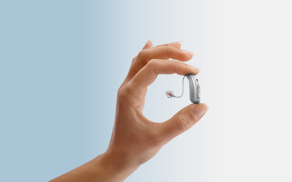 Hand holding hearing aid between thumb and forefinger