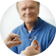 older man looking at hearing aid in hand