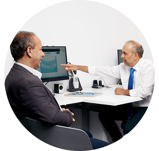Image shows man talking to audiologist in front of a screen showing an audiogram